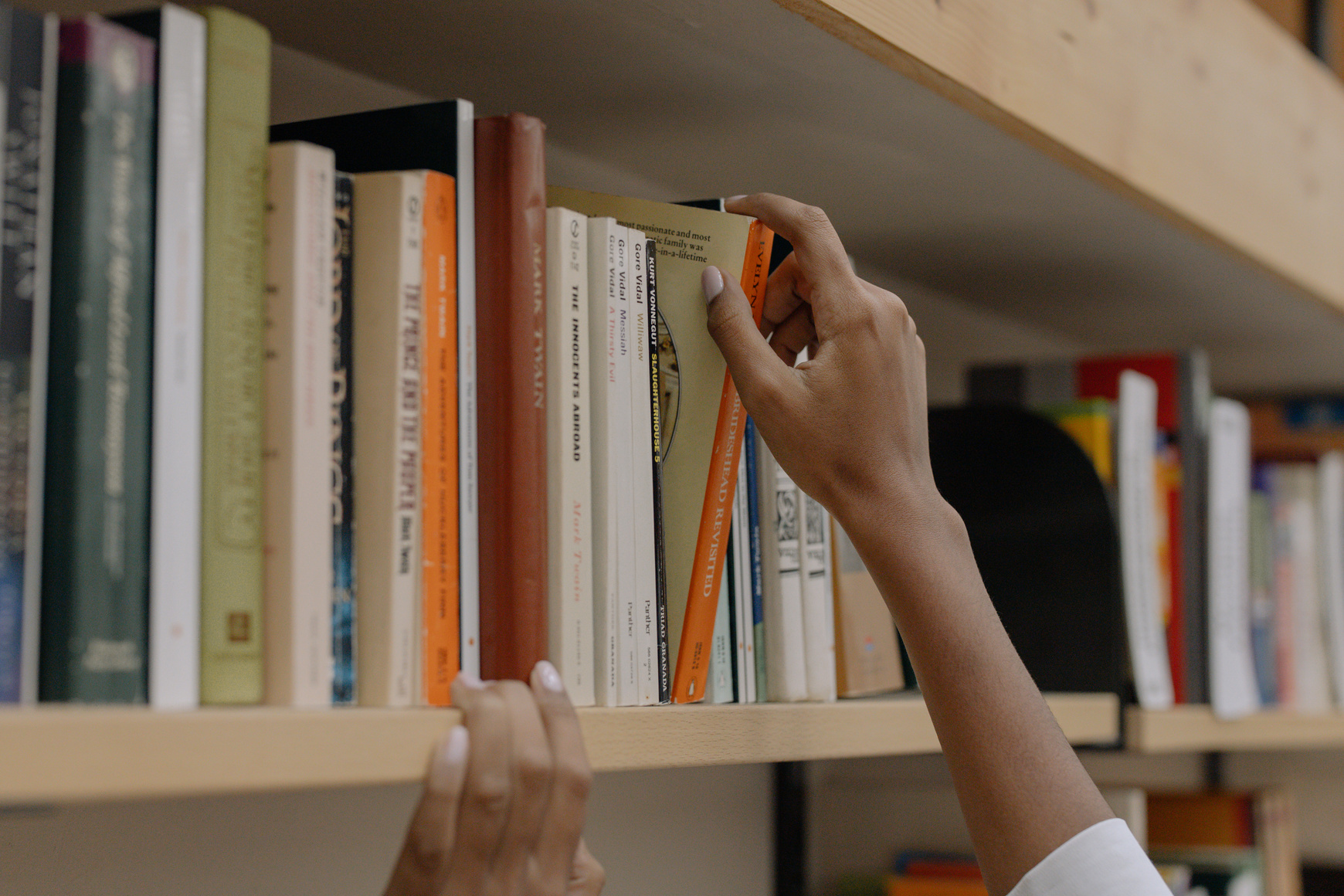 Person Holding A Book On Wooden Shelf